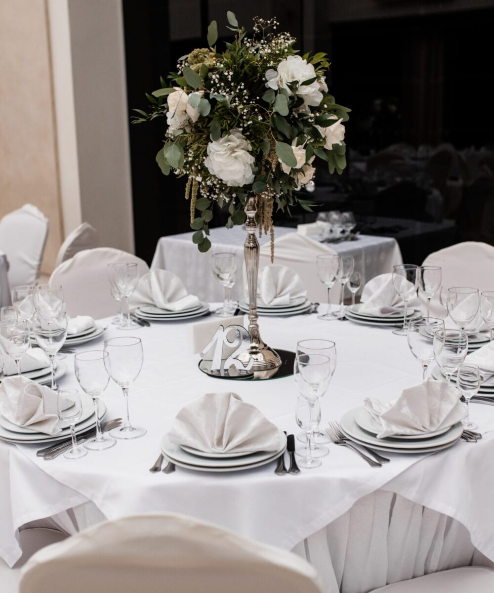 podawany w restauracji bialy okragly stol z kwiatowym elementem centralnym scaled